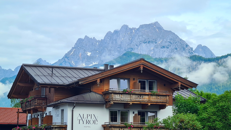 A hotel in St Johann in Tirol with neat window boxes. Behind our the peaks of the Wilder Kaiser Mountains